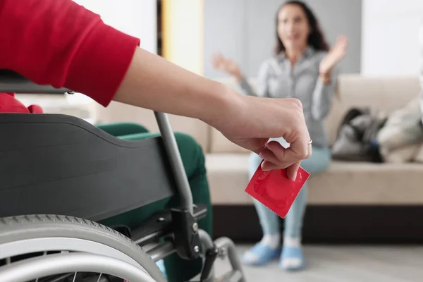 Людина сидить у інвалідному кріслі тримає червоний презерватив в руці перед жінкою, сидячи — стокове фото