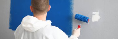 Elinde silindir olan bir adam duvarı maviyle boyuyor..