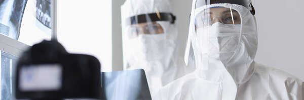 Врачи в защитных экранах и противочумных костюмах смотрят в камеру в рентгеновском кабинете