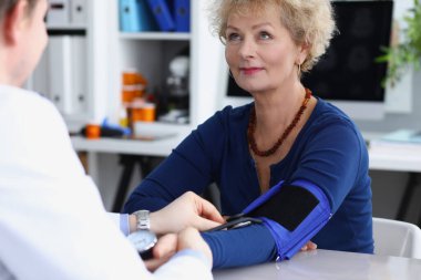 Doktor muayenehanedeki yaşlı bir kadının kan basıncını ölçüyor.