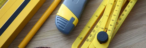 Construction level, knife, pencil, tape measure for performing and controlling construction work lie on brown table.