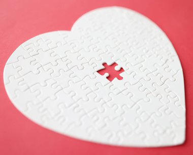 Kırmızı arka planda duran yapbozdan yapılmış beyaz kalp