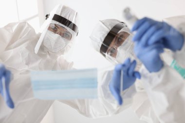 Koruyucu giysiler içindeki doktorlar hasta maskesi takıyor ve sıcaklığı ölçüyorlar.