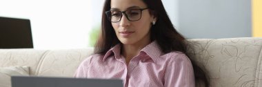 Gözlüklü kadın kanepeye oturur ve dizüstü bilgisayara bakar..