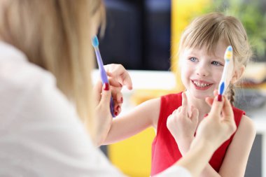 Klinikteki doktorların ellerinden diş fırçasını seçen küçük kız.