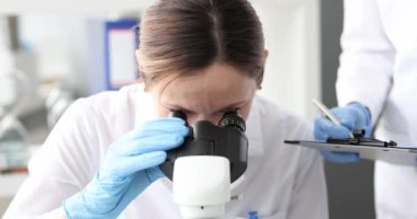 Kadın biyolog mikroskop 4k filminde asistan örneği gösteriyor.