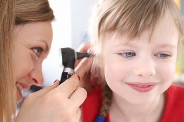 Otorhinolarbilimi uzmanı küçük bir kızın kulağına bakıyor.