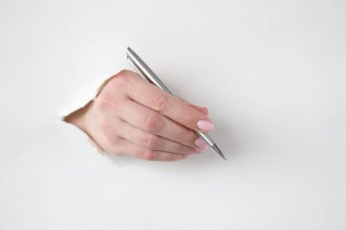 Kadın eli kalemi beyaz kağıttaki delikten tutuyor.