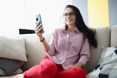 Kanepede oturan ve akıllı telefona bakan gülümseyen kadın.