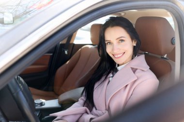 Gülümseyen kadın modern kahverengi araba portresine oturur.