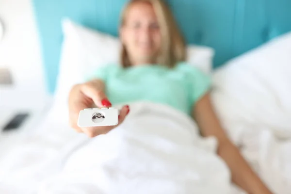 Mujer acostada en la cama presiona botones en el control remoto —  Fotos de Stock