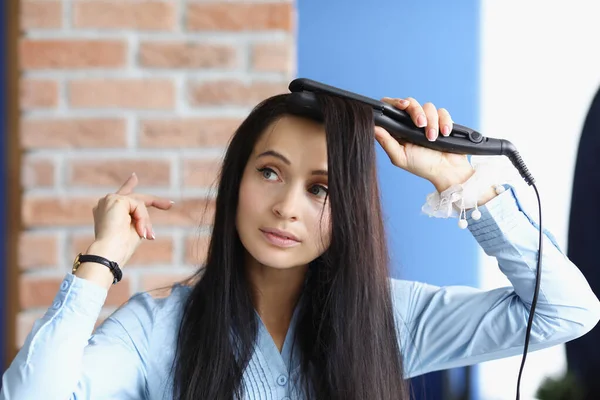 Brunett kvinna gör curling av hennes hår med locktång — Stockfoto