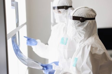 Koruyucu giysili ve maskeli iki doktor röntgeni inceliyor.