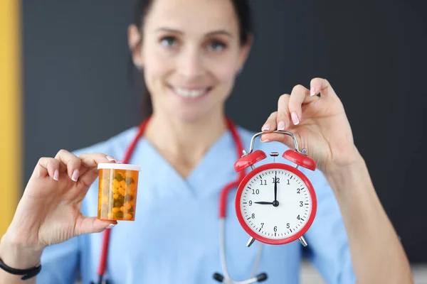 Smiling doctor holds red alarm clock and medication in his hand — Stock Photo, Image