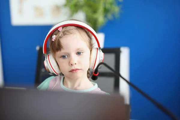 Kulaklıklı küçük kız mikrofonlu monitörün önünde oturuyor. — Stok fotoğraf