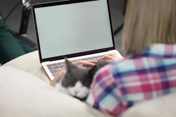 Woman is sitting on couch with laptop and cat
