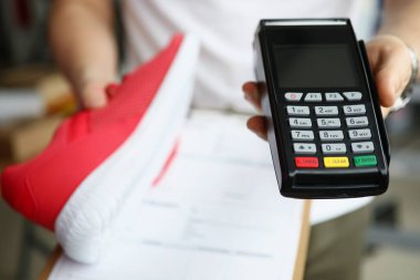 Adamın elinde spor ayakkabıları ve ödeme terminali konsepti var.