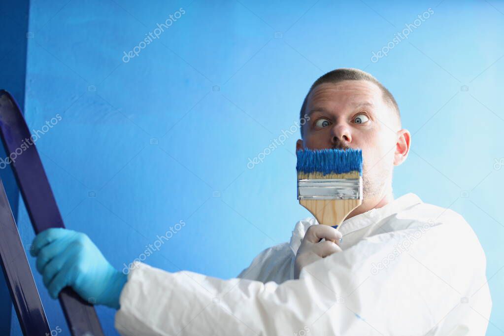 Male painter holds paintbrush near his face