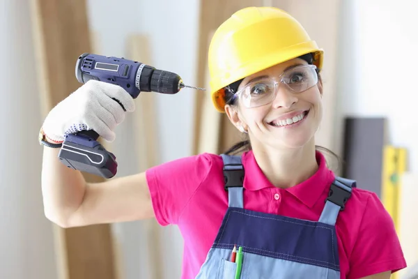 Mujer sonriente constructora sostiene taladro cerca de su cabeza —  Fotos de Stock