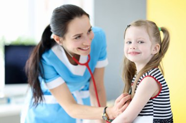 Gülümseyen doktor steteskopla küçük kızın nefesini dinler.