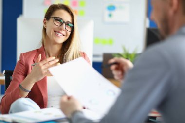 Ofisteki meslektaşıyla iletişim kuran gözlüklü, gülümseyen iş kadını.
