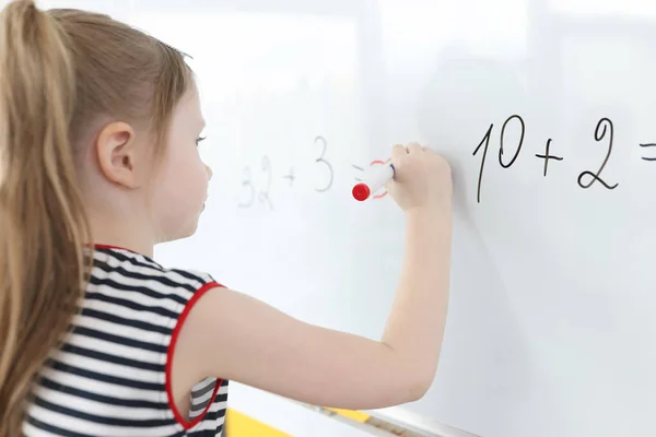 Little girl writes math examples on white board — Stock Photo, Image