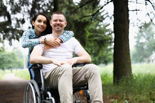 Ung kvinna kramar handikappad man i rullstol i parken — Stockfoto