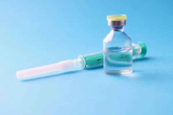 Närbild av glasburk med medicin och steril spruta på blå bakgrund — Stockfoto