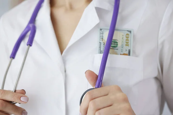 Doctor with dollar bills in his pocket holding stethoscope closeup