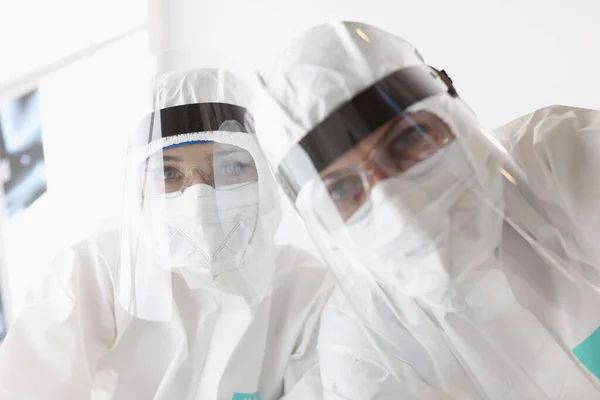 Doctors in protective antiplague suits and screens looking at patient