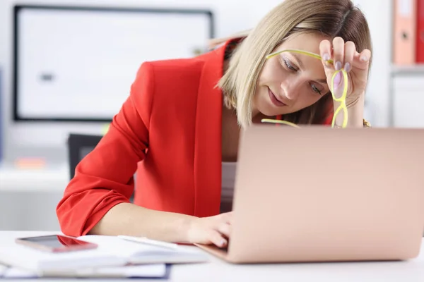 Moe vrouw zittend achter laptop met bril in haar handen — Stockfoto