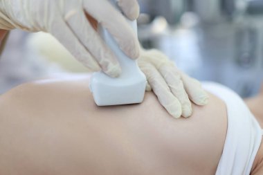 Doktor, kadının meme bezlerini ultrason ile muayene ediyor.