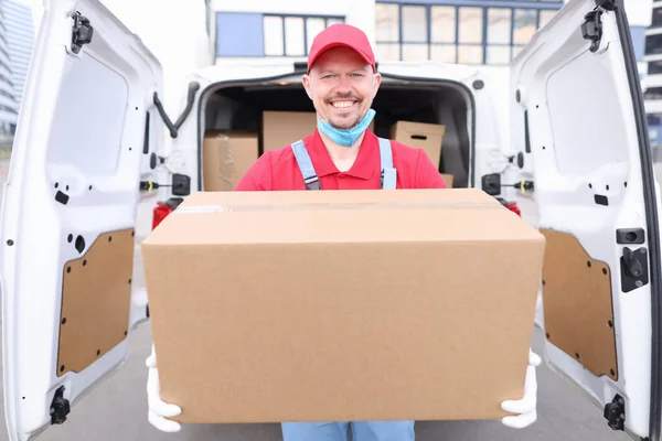 Man courier holds cardboard box on background of car