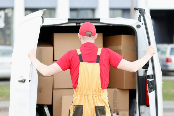 Male courier stands behind car with open doors in cardboard box showroom — Stock Photo, Image