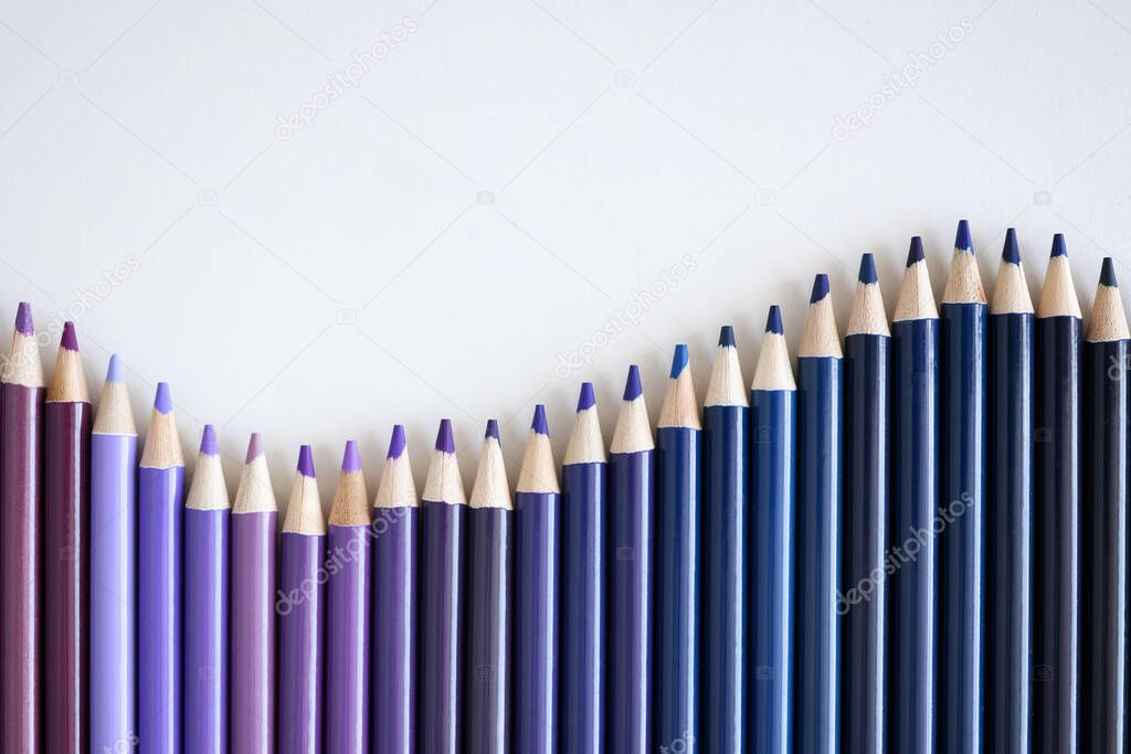 Many shades of blue and purple pencils lying on white background closeup