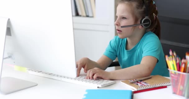 Κοριτσάκι με ακουστικά πληκτρολογεί στο πληκτρολόγιο του υπολογιστή και κοιτάζοντας την οθόνη 4k ταινία — Αρχείο Βίντεο