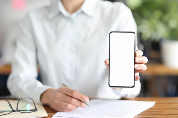 Zakelijke vrouw zit aan tafel met documenten en toont mobiele telefoon closeup — Stockfoto