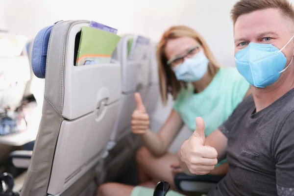 Man och kvinna i skyddande medicinska masker flyger i flygplan och visar tummen upp — Stockfoto