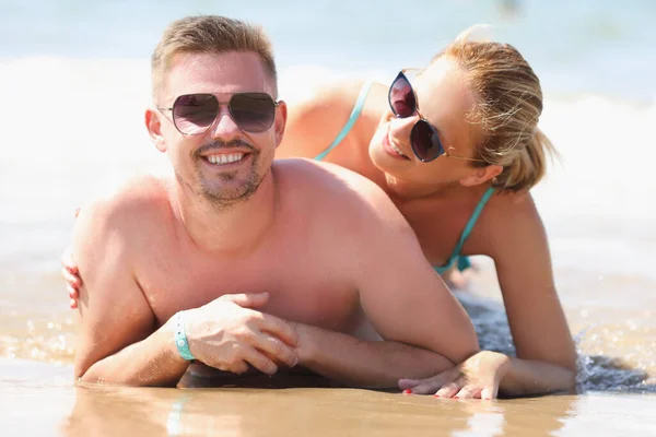 Giovane uomo e donna in occhiali da sole sdraiati sulla riva del mare — Foto Stock