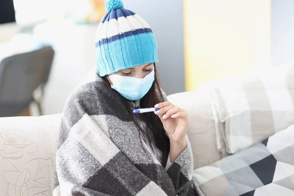 Frau mit Mütze und Schutzmaske blickt auf Thermometer — Stockfoto