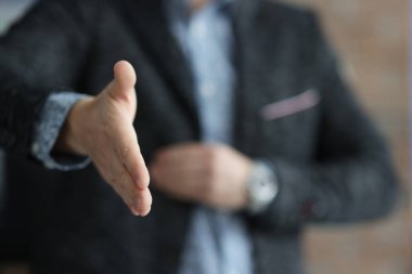Siyah ceketli bir adam elini uzatıyor ve yakın çekim için elini uzatıyor.
