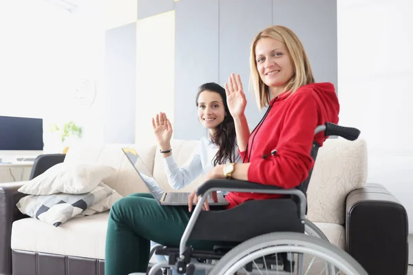 Жінка в інвалідному візку сидить з ноутбуком і махає рукою — стокове фото