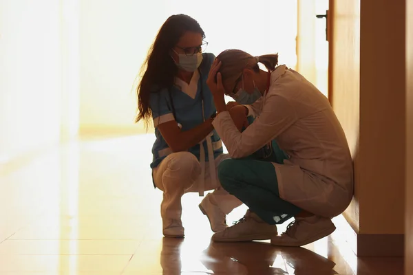 Médicos cansados em máscara médica protetora sentam-se no corredor — Fotografia de Stock