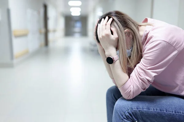 Mulher perturbada em máscara médica protetora senta-se no corredor hospitalar — Fotografia de Stock