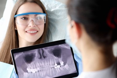 Diş hekimi elinde dijital tablet tutuyordu. Kadın hastaların önünde dişlerinin 3 boyutlu fotoğrafı vardı.