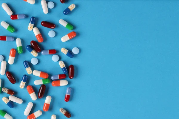 Muchas cápsulas y píldoras médicas multicolores que yacen sobre fondo azul — Foto de Stock