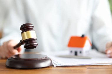 Judge holds judge wooden gavel against background of house and documents