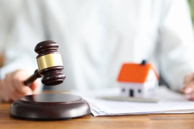 Judge holds judge wooden gavel against background of house and documents clipart