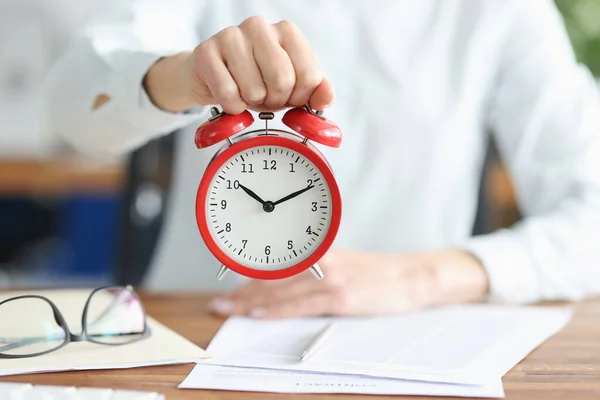 Female hand holds red alarm clock at working table — стоковое фото