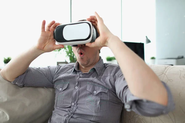 Überraschter Mann mit Virtual-Reality-Brille sitzt zu Hause auf Couch — Stockfoto